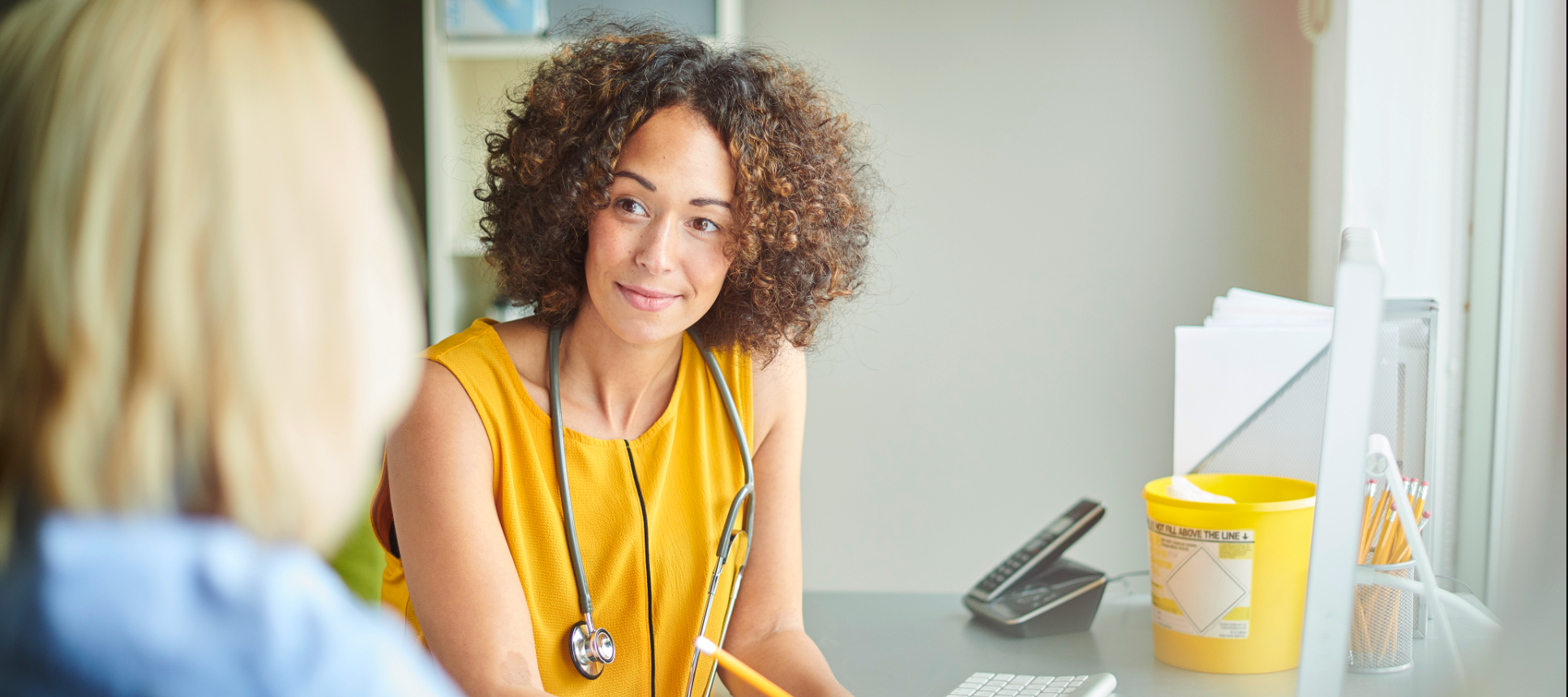 Young female doctor in yellow shirt talking to patient.