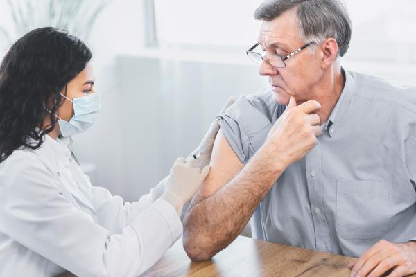 Nurse giving imunisation injection to older male patient