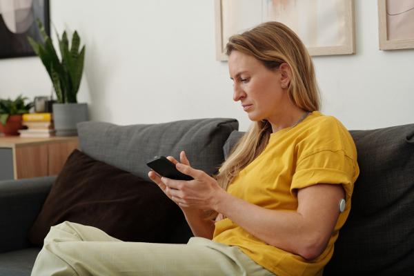 Woman wearing a CGM checking her blood glucose level on her mobile phone