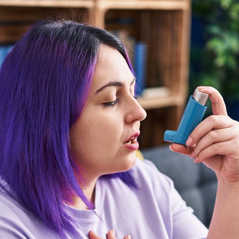middle aged overweight woman with purple hair using an inhaler