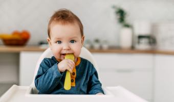 baby sitting in high chair with yellow spoon in the kitchen