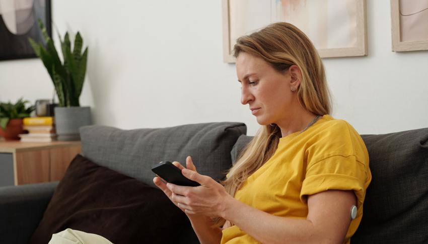 Woman wearing a CGM checking her blood glucose level on her mobile phone