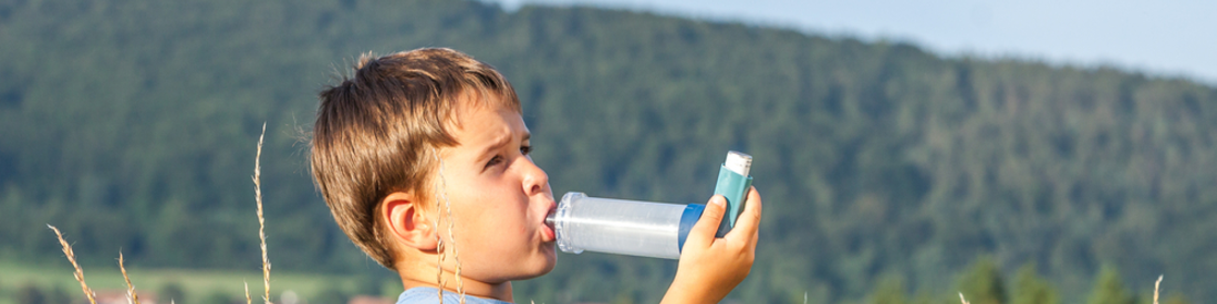 Young child in an open field using an inhaler with spacer